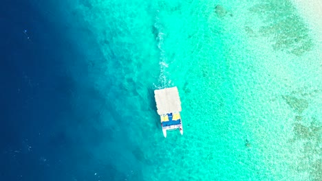 Small-boat-sailing-near-the-coral-reef-Malaysia,-aerial-overhead-motion-background