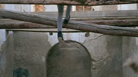 Young-man,-teenager,-swings-his-feet-sitting-several-meters-high-on-a-collapsed-beam-in-an-abandoned-house