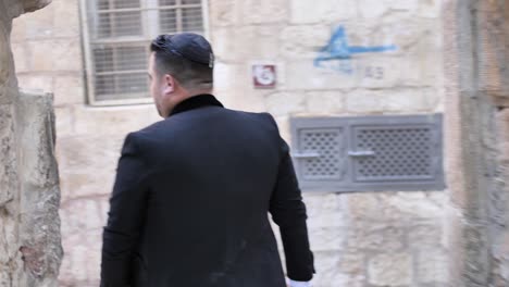 Jewish-man-walks-the-narrow-street-in-Jerusalem,-sign,-inscription-on-the-wall