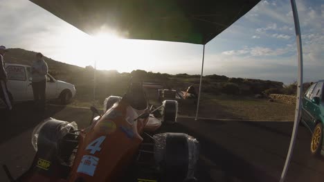 Brand-New-Racing-Car-Parked-Under-The-Tent-At-The-Roadside-Of-The-Hill-In-Imtahleb-Malta-With-Wheels-Covered-With-Plastic---GoPro-Pan-Shot