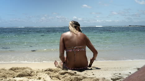 Rear-view-shot-of-female-person-at-shore-of-sandy-beach-playing-with-piece-of-wood