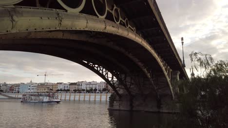 Tilt-Down-shot-from-Iconic-Triana-Bridge-to-River-Boat-Tour-in-Seville,-Spain
