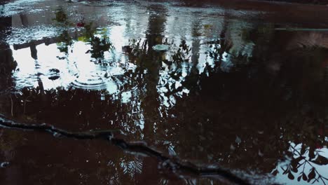 Herbstliche-Regenwassertropfen-Fallen-In-Eine-Pfütze-Auf-Dem-Bürgersteig,-Nahaufnahme-In-Zeitlupe