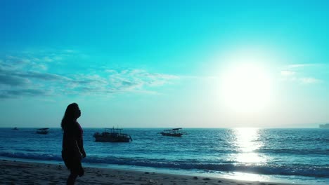 Young-woman-watching-beautiful-sunset-with-glowing-sun-reflecting-on-calm-sea-surface,-silhouettes-of-anchored-fishing-boats,-Bali