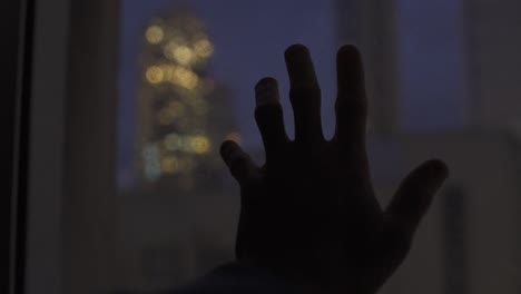 Hand-rests-on-window-with-view-to-the-city-at-night-time
