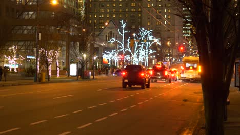 Cars-driving-on-a-street-with-outdoor-lights-in-trees-in-downtown-Vancouver-at-evening-in-winter-time
