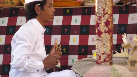 Sacerdote-Hindú-Vestido-De-Blanco-Sosteniendo-Un-Objeto-Religioso-Reza-En-Un-Altar-Colorido-De-Un-Templo-En-Bali,-Indonesia