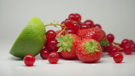 A-Slice-Of-Lime,-Three-Sweet-Strawberries-And-A-Bunch-Of-Red-Currants-On-Top-Of-The-Table---Close-Up-Shot