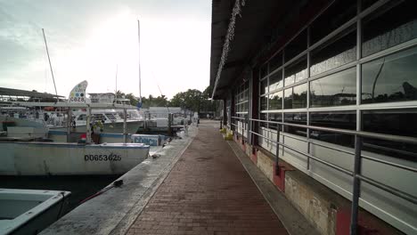 Wide-Shot-Tracking-Down-Sidewalk-of-Marina-With-Boats-Docked-in-Water