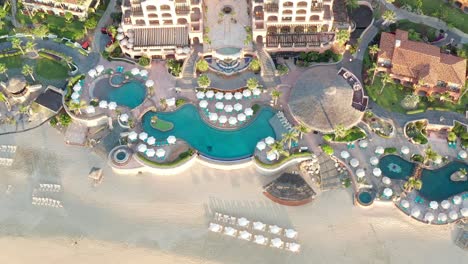 Aerial,-tilt-up,-drone-shot,-away-from-the-Sheraton-hotel-and-a-beach,-revealing-resorts-and-buildings,-in-Cabo-San-Lucas,-on-a-sunny-day,-in-Baja-Peninsula,-Mexico
