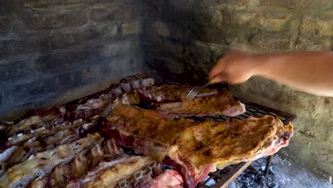 Man-hands-moving-around-pieces-of-beef-meat-in-Argentinian-asado-to-cook-evenly