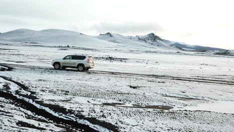 Toyota-Highlander-Fourwheeler-SUV-Moving-in-Amazing-Landscape-of-Highlands-of-Iceland,-Snow-Capped-Hills-and-Valley-in-Fjallabak-Nature-Reserve