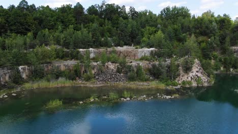 Aerial-View-of-lake-with-Beautiful-Water-in-a-Quarry-Surrounded-by-Forest-Tracking-Backward