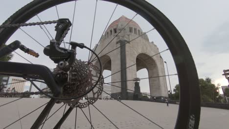 Rueda-De-Bicicleta-Girando-Con-El-Monumento-A-La-Revolución-Al-Fondo-En-Cámara-Lenta,-Ciudad-De-México