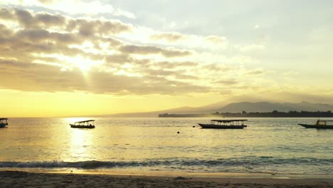 Heller-Himmel-Mit-Wunderschönen-Wolken,-Die-über-Der-Ruhigen-Meeresoberfläche-Hängen-Und-Die-Gelben-Farben-Eines-Romantischen-Sonnenuntergangs-Reflektieren,-Verankerte-Boote-In-Der-Bucht-Von-Bali