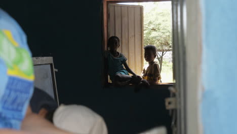 Two-Ziway-kids-standing-by-classroom's-window,-looking-at-camera-while-two-volunteers-paint-walls-in-foreground