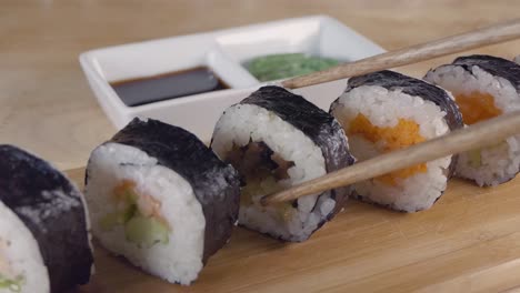 Slow-Motion-Slider-Shot-of-Taking-a-Piece-of-Sushi-From-a-Wooden-Serving-Board-with-Chopsticks