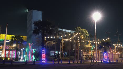 Medium-still-zoom-out-Shot-Of-Colorful-Amusement-Park-made-out-of-containers-with-People-Walking-in-Front-of-it-in-the-Night-Time