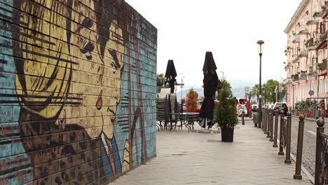 Urban-graffiti-on-wall-by-street-with-city-traffic-going-past-in-Batumi,-Georgia