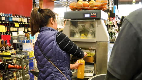 Woman-uses-orange-press-machine-in-store-to-make-fresh-orange-juice,-Vine-Ripe-Market