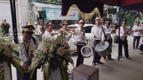 A-brass-band-dressed-in-French-Colonial-uniform-play-loud-music,-an-important-ritual,-at-a-funeral-in-a-narrow-urban-street-in-Vietnam