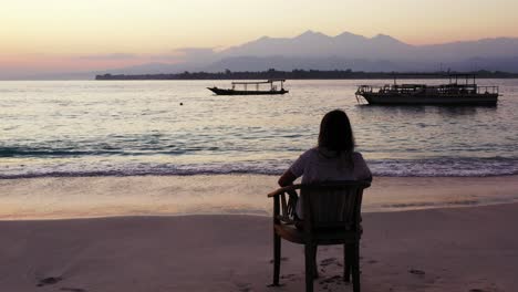 Silhouette-of-woman-sitting-on-exotic-beach,-watching-romantic-sunset-with-beautiful-colorful-light-reflecting-on-sea-surface,-Bali