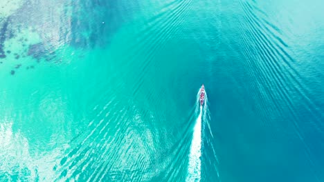 Boat-sailing-slowly-on-calm-turquoise-sea-surface-reflecting-sunlight-near-shore-of-tropical-island-with-coral-reefs-on-seabed-in-Cambodia