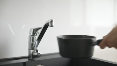 Male-hands-fill-small-black-cooking-pot-with-water-by-silver-faucet