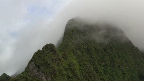Aerial-static-shot-of-low-altitude-clouds-rolling-over-a-mountain-peak-covered-by-lush-vegetation