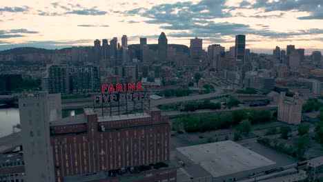 Drone-flying-away-from-the-famsous-flshing-red-sign-of-the-Farine-Five-Roses-building,-with-Montreal-downtow-in-the-background