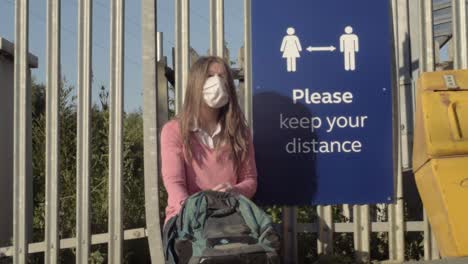 Woman-wearing-mask-looking-in-bag-near-to-social-distancing-sign-wide-shot