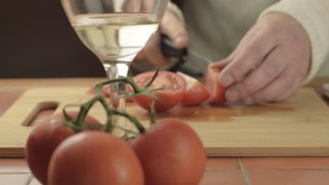 Hands-cutting-fresh-vine-tomatoes-in-kitchen-with-glass-of-white-wine-medium-shot