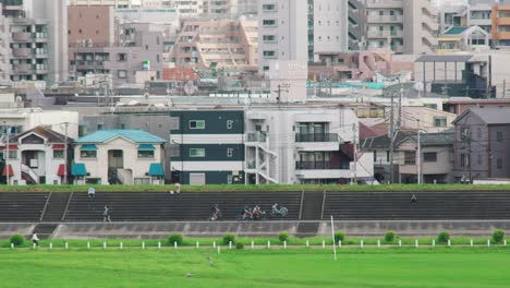 Japaner-Radeln-Tagsüber-In-Tokio,-Japan,-Entlang-Der-Berme-Am-Tamagawa-Fluss-Mit-Wohngebäuden-Im-Hintergrund