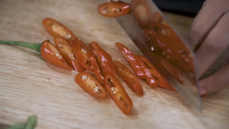 Cutting-a-Red-Chili-Pepper-into-Slices-with-Knife-on-Wooden-Chopping-Board---Close-Up