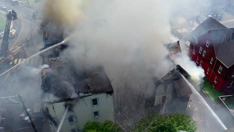 Rauch-Füllt-Die-Luft-Nach-Einem-Brand-In-Einem-Wohnhaus,-Feuerwehrleute-Sind-Vor-Ort-Und-Schwenken-Eine-Drohnenaufnahme