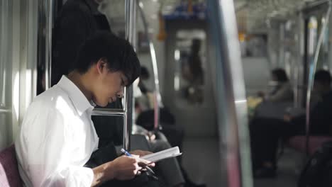 Estudiante-De-Secundaria-Japonés-Estudiando-Mientras-Viaja-En-El-Tren-En-Tokio,-Japón
