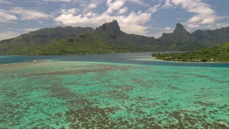Aerial-establishing-shot-of-Mo'orea-island,-flying-over-the-barrier-reef-and-stunning-mountains-on-background