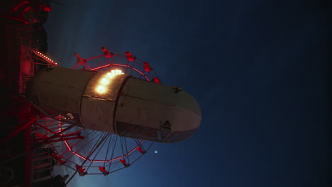 Satellite-ride-spinning-in-front-of-ferris-wheel-at-carnival-at-night,-Wide-Shot,-Slow-Motion