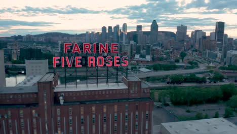 Drone-moving-down-in-front-of-the-flashing-red-neon-sign-of-the-Farine-Five-Roses-building-in-Montreal,-Quebec
