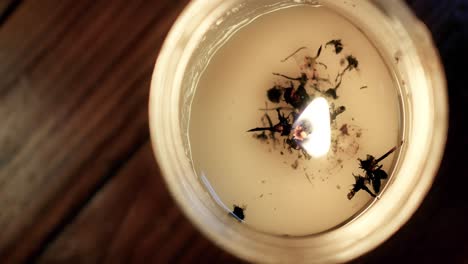 Top-view-close-up-of-white-prayer-candle-with-dark-potpourri-flickering-on-a-dark-wood-floor