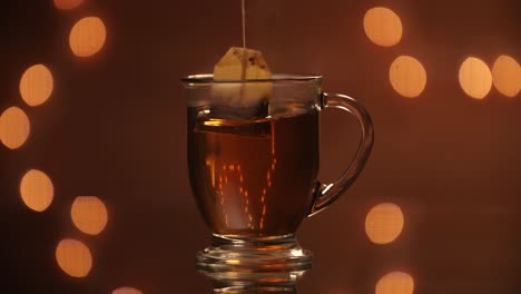 Black-tea-back-being-dunked-throughout-a-steaming-glass-mug-on-a-beautiful-bokeh-backdrop