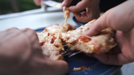 Close-up-of-hands-taking-homemade-pizza-slices-with-a-lot-of-cheese-on-it