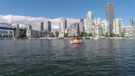 birds-fly-over-a-reflective-ocean-harbor-of-Granville-Island,-yaletown,-the-burrard-bridge-with-whale-watching-boats-docking,-bbq-boat-passing-by-at-the-most-luxurious-modern-architecture-of-towers1-2