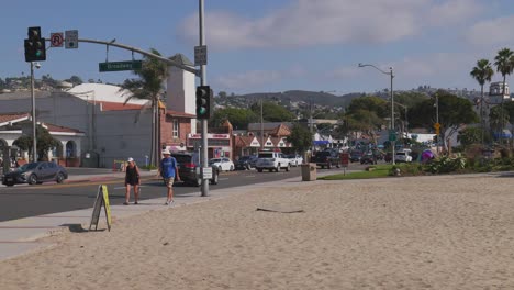 A-couple-walking-along-Pacific-Coast-Highway,-as-they-pass-Broadway-in-laguna-Beach,-California