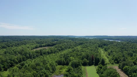 Drone-flies-over-green-trees,-farmland-and-brown-lakes-before-revealing-beautiful-Potomac-River,-Maryland
