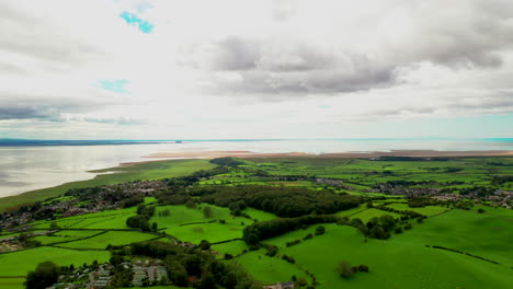 Aerial-view-of-lush-green-farmland-on-the-coastline-of-England,-bright-sunshine
