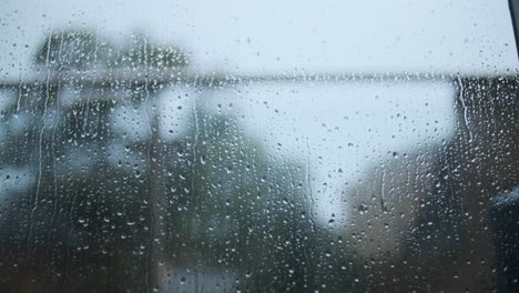 Raindrops-falling-down-glass-window-trees-in-background