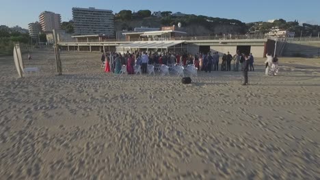 Small-wedding-ceremony-right-on-the-beach-shore,-aerial-pull-in-shot