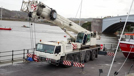 Hydraulic-crane-vehicle-raising-boom-arm-to-move-fishing-boat-on-Conwy-Wales-harbour