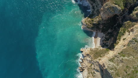 Luftaufnahme-Von-Oben-Nach-Unten-Auf-Einen-Wunderschönen-Strand-Mit-Türkisfarbenem-Wasser-Zwischen-Den-Klippen-An-Der-Mittelmeerküste-Spaniens